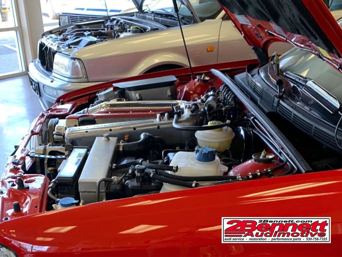 Clean engine bay of a red Audi S2 with the hood up in the 2Bennett showroom